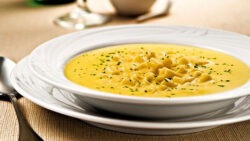 Imagem de um prato com uma porção de sopa de mandioquinha, ao lado uma colher.